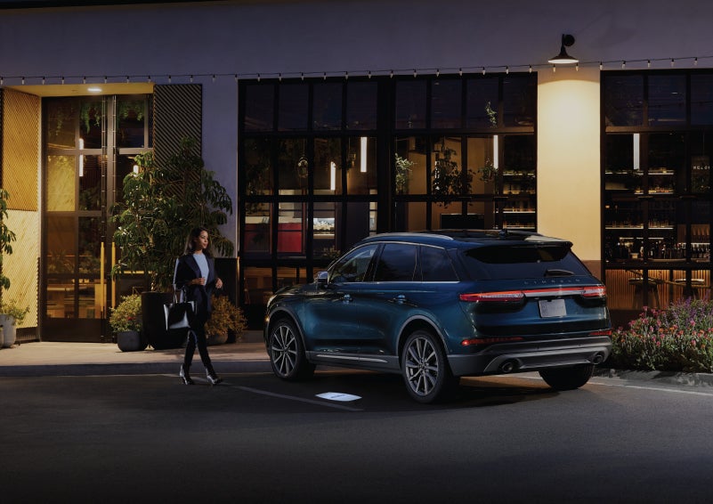 A driver approaches a 2022 Lincoln Corsair SUV in Flight Blue at night greeted by the soft glow of the Lincoln Embrace | Performance Lincoln Bountiful in Bountiful UT