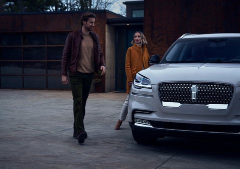 A man and a woman approaching a 2024 Lincoln Aviator® SUV, which illuminates certain lights when they are close | Performance Lincoln Bountiful in Bountiful UT